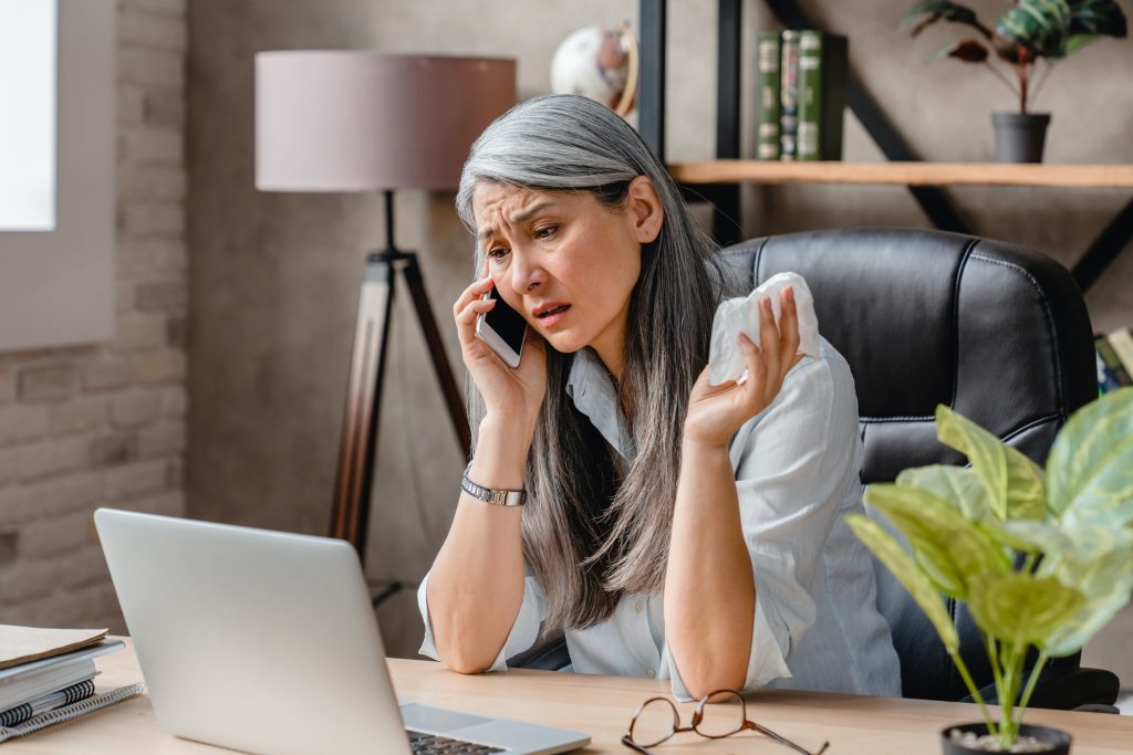 Attractive middle-aged woman asking for sick leave on the phone at the working place